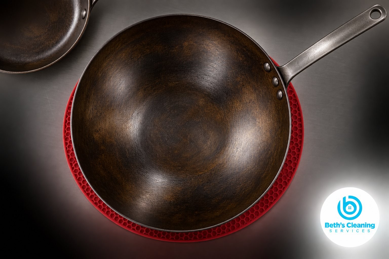 Seasoned carbon steel wok on a red trivet with a skillet on a stainless steel counter
